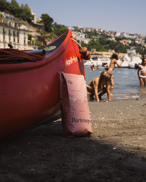 Confezione Sirena Caffè Partenope in spiaggia accanto a una canoa